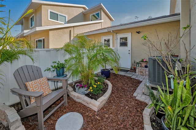 property entrance featuring central air condition unit, stucco siding, and fence