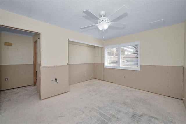 unfurnished room featuring a wainscoted wall, a textured ceiling, and ceiling fan