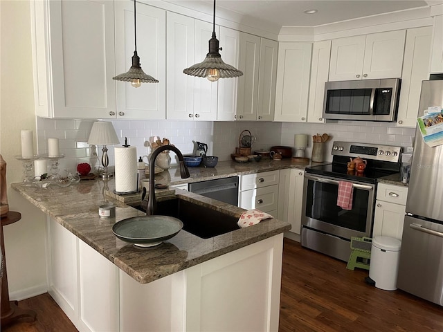 kitchen featuring dark wood-type flooring, a sink, dark stone countertops, stainless steel appliances, and a peninsula