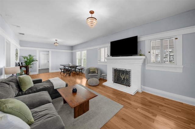 living room featuring a brick fireplace, an inviting chandelier, and light hardwood / wood-style floors