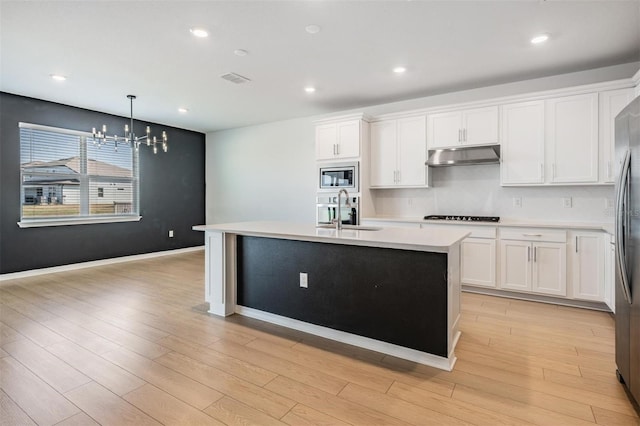 kitchen with sink, hanging light fixtures, stainless steel appliances, white cabinets, and a center island with sink