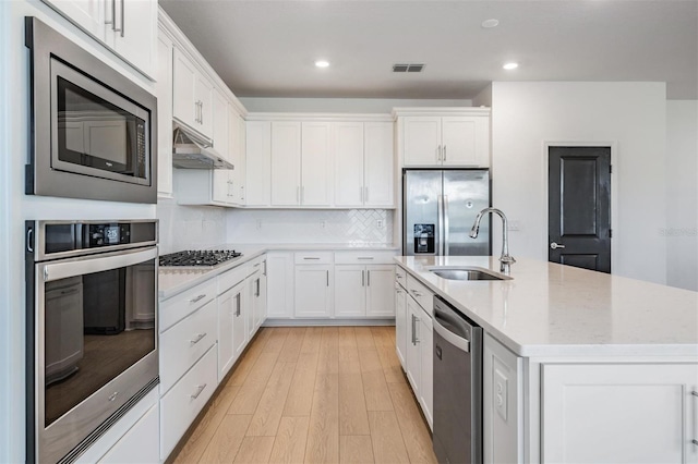 kitchen with sink, appliances with stainless steel finishes, backsplash, white cabinets, and a center island with sink