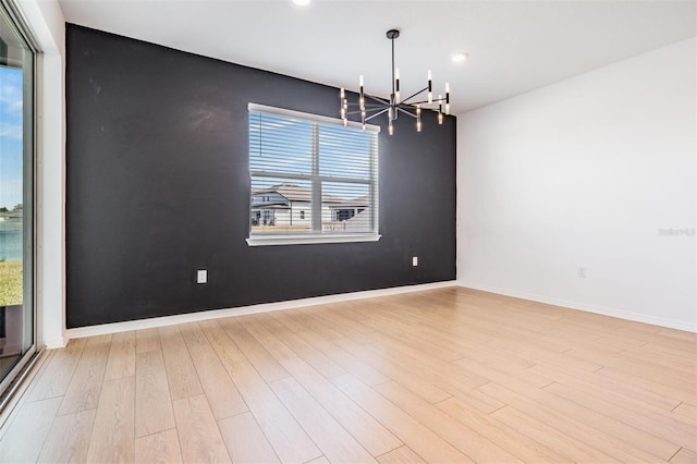 unfurnished room featuring a notable chandelier and light wood-type flooring