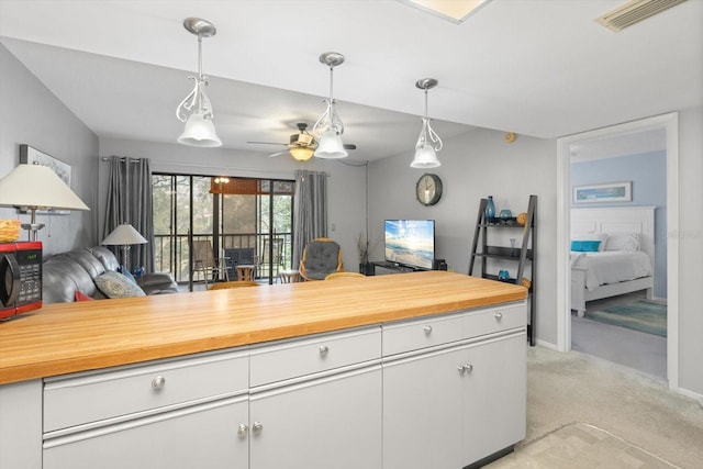 kitchen featuring wood counters, decorative light fixtures, light colored carpet, and white cabinets