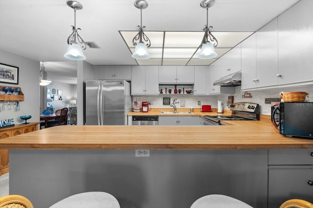 kitchen with appliances with stainless steel finishes, sink, white cabinets, hanging light fixtures, and kitchen peninsula