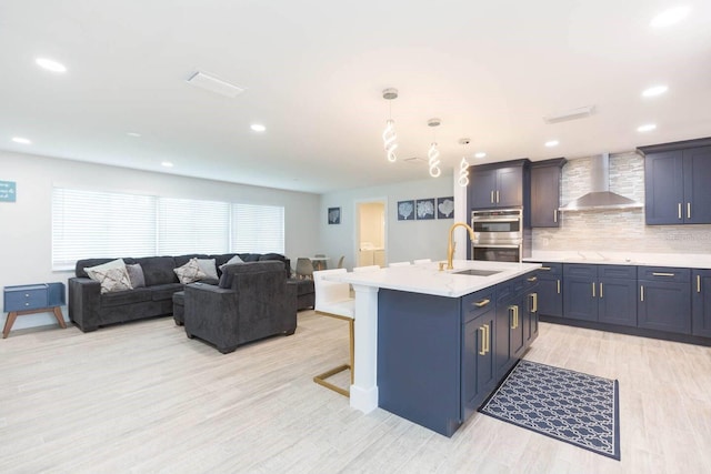 kitchen with a kitchen bar, sink, pendant lighting, a kitchen island with sink, and wall chimney range hood