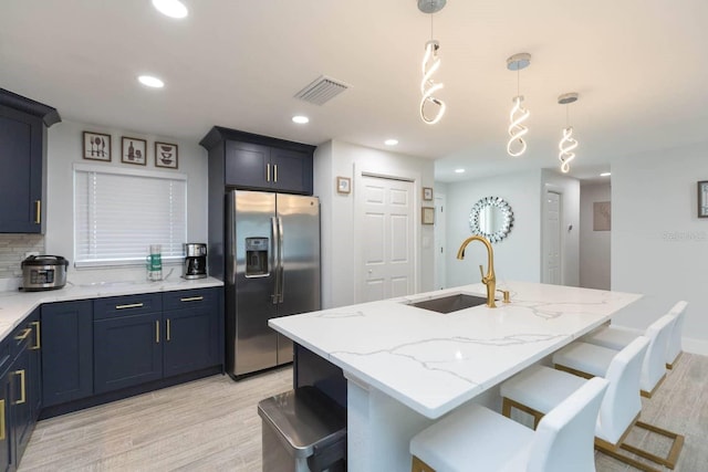 kitchen featuring pendant lighting, sink, stainless steel fridge, a kitchen breakfast bar, and a center island with sink