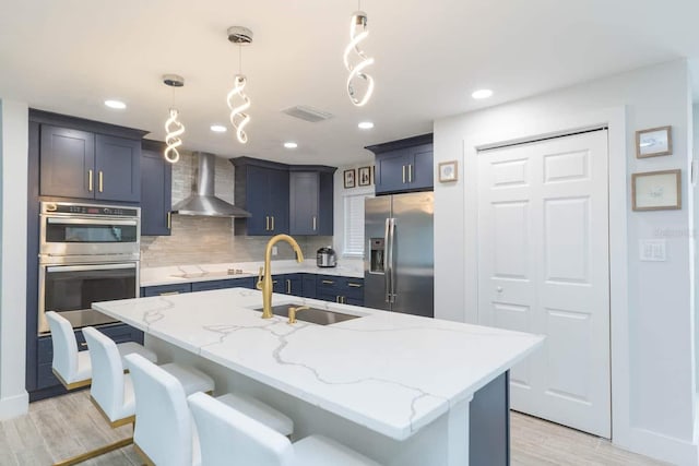 kitchen featuring an island with sink, appliances with stainless steel finishes, sink, and wall chimney range hood