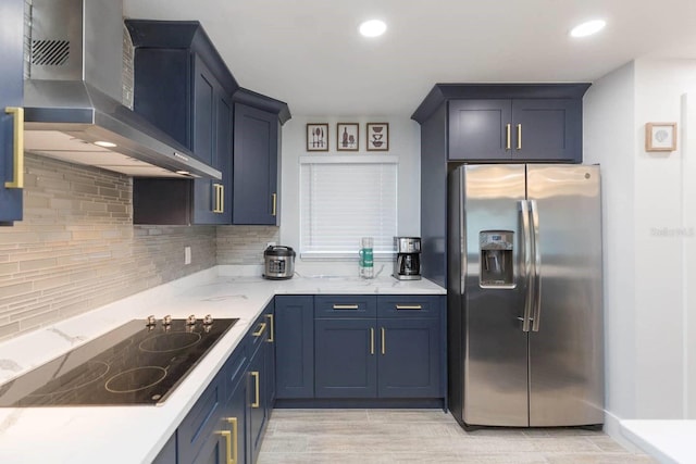 kitchen featuring wall chimney range hood, stainless steel refrigerator with ice dispenser, tasteful backsplash, blue cabinets, and black electric cooktop