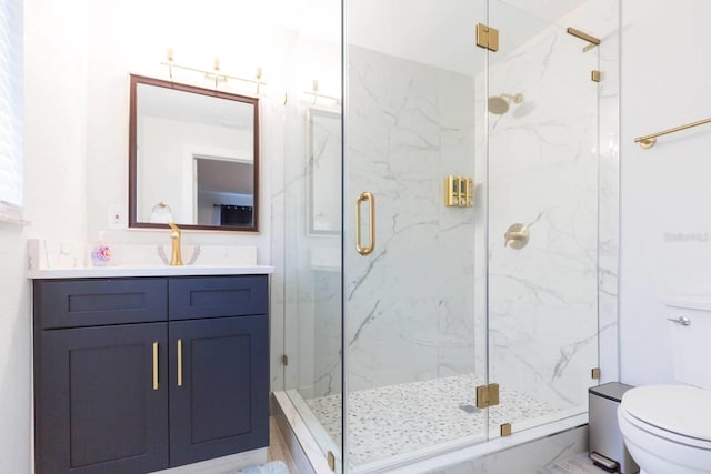 bathroom featuring a shower with door, vanity, and toilet