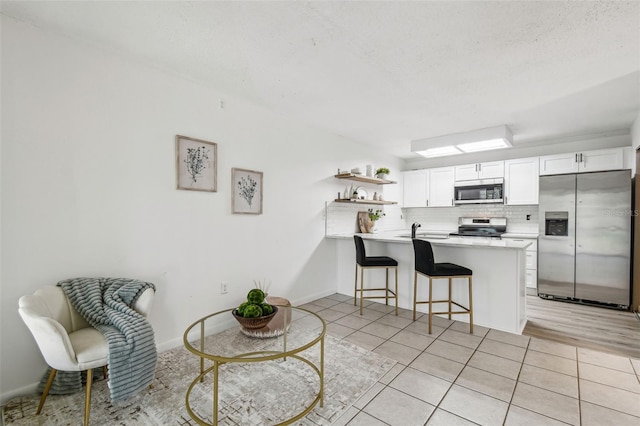 kitchen featuring white cabinets, a kitchen bar, light tile patterned floors, kitchen peninsula, and stainless steel appliances