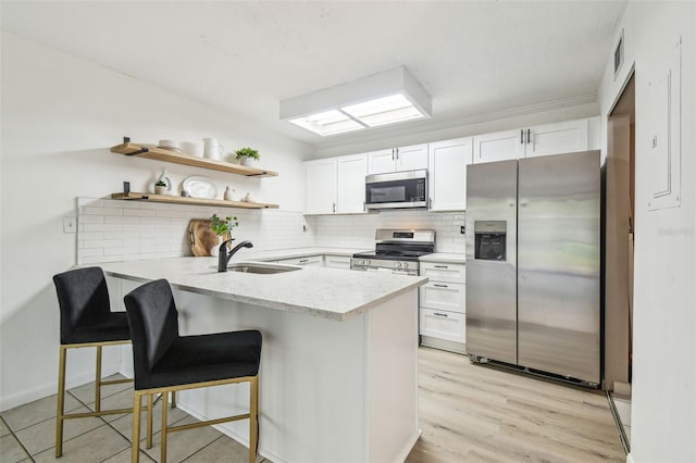 kitchen with appliances with stainless steel finishes, sink, white cabinets, and kitchen peninsula