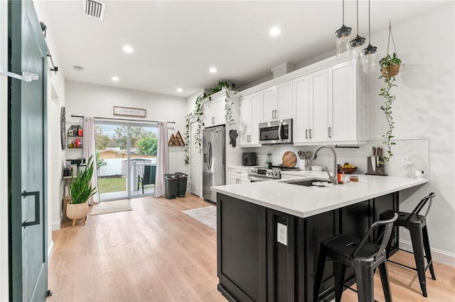 kitchen with a kitchen bar, white cabinetry, appliances with stainless steel finishes, kitchen peninsula, and pendant lighting