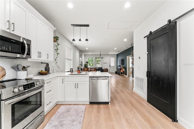 kitchen with sink, appliances with stainless steel finishes, kitchen peninsula, white cabinets, and a barn door