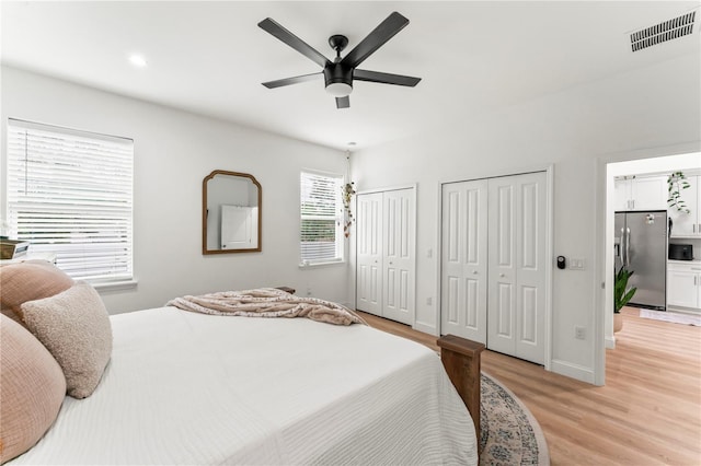 bedroom featuring light hardwood / wood-style flooring, two closets, ceiling fan, and stainless steel fridge with ice dispenser