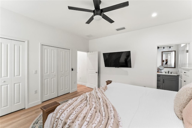 bedroom featuring connected bathroom, two closets, sink, ceiling fan, and light wood-type flooring