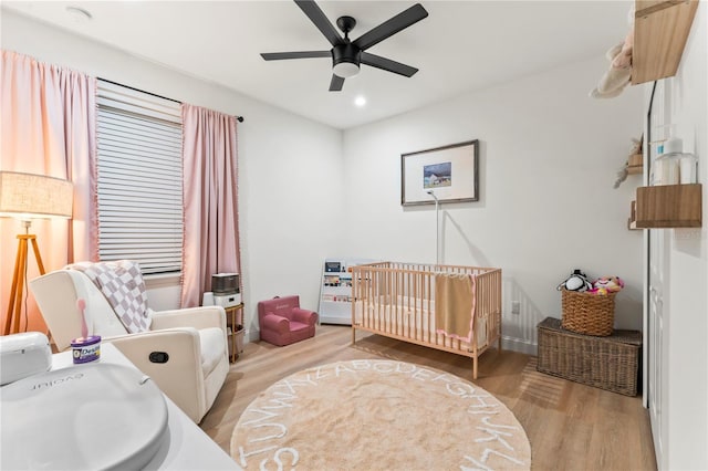 bedroom with a nursery area, ceiling fan, and light wood-type flooring