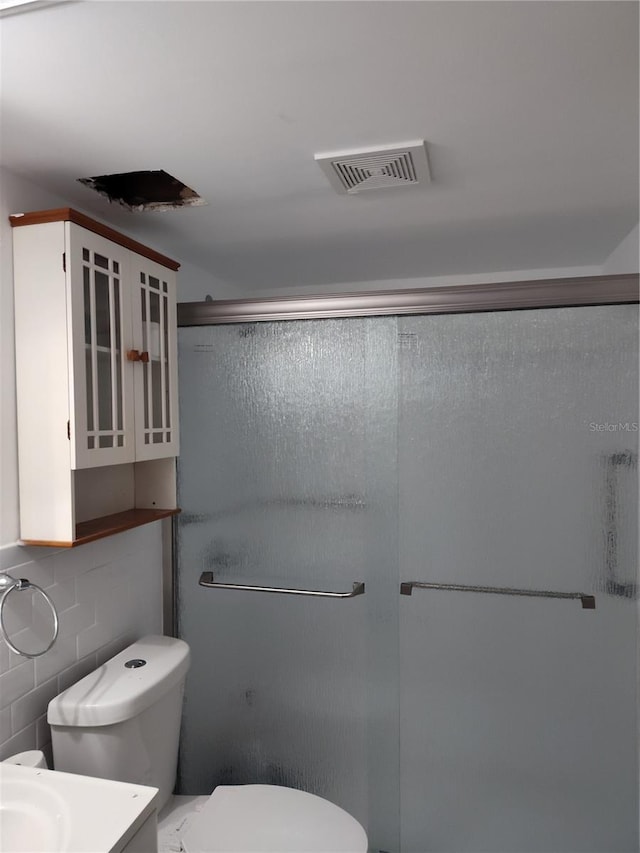 bathroom featuring vanity, toilet, a shower with shower door, and tile walls