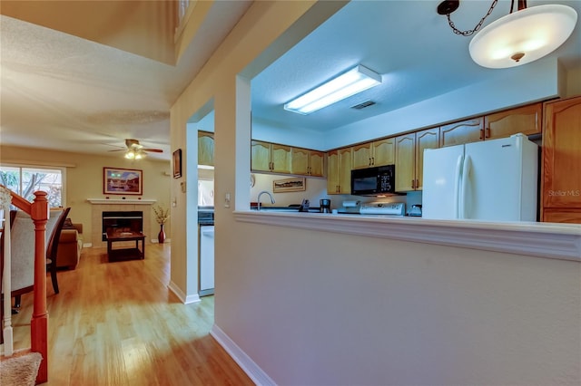 kitchen featuring a tile fireplace, sink, white refrigerator, hanging light fixtures, and light hardwood / wood-style flooring