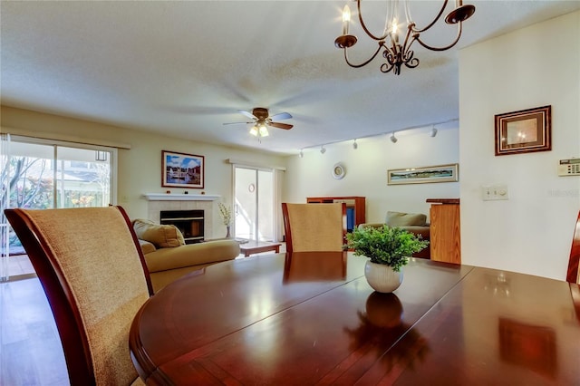 dining area featuring rail lighting, a tiled fireplace, ceiling fan with notable chandelier, and a textured ceiling