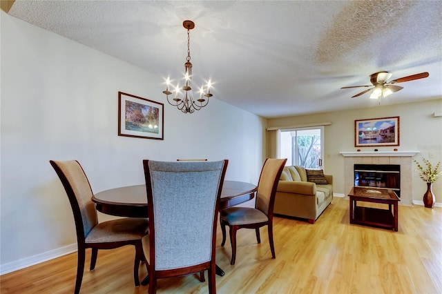 dining space featuring ceiling fan with notable chandelier, a tile fireplace, light hardwood / wood-style flooring, and a textured ceiling