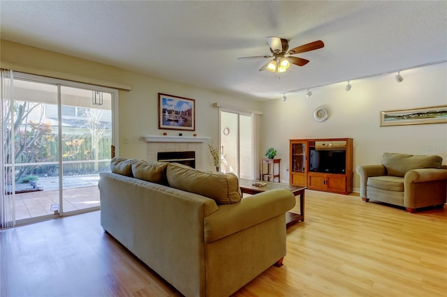 living room with ceiling fan, rail lighting, a tile fireplace, and light wood-type flooring