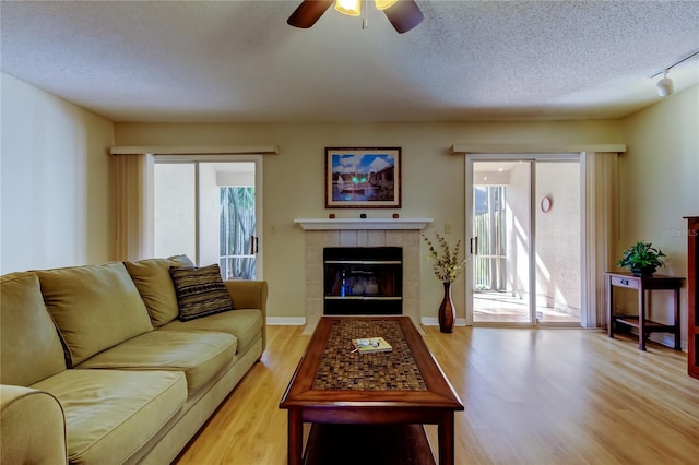 living room featuring a healthy amount of sunlight, a tile fireplace, light hardwood / wood-style flooring, and a textured ceiling