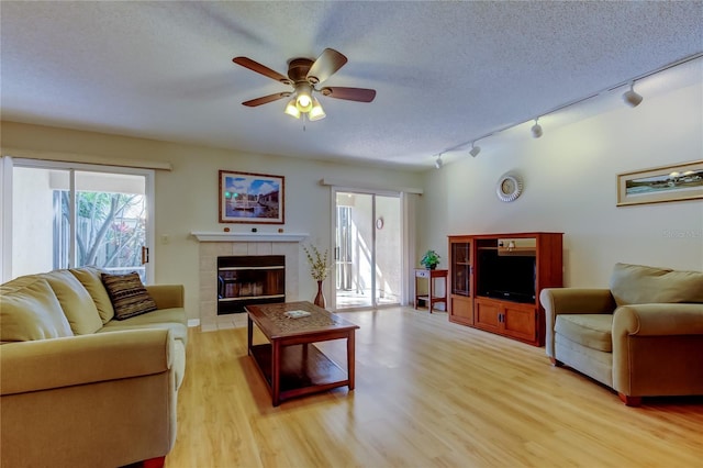 living room featuring ceiling fan, a tiled fireplace, a textured ceiling, and light hardwood / wood-style flooring