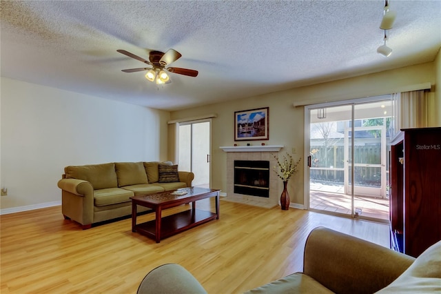 living room with ceiling fan, a fireplace, a textured ceiling, and light wood-type flooring