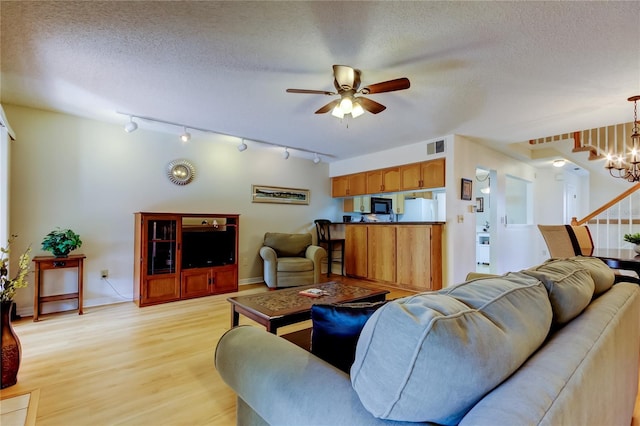 living room featuring ceiling fan with notable chandelier, a textured ceiling, and light hardwood / wood-style flooring