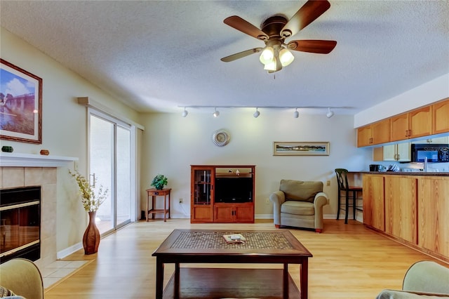 living room featuring a tiled fireplace, a textured ceiling, and light wood-type flooring