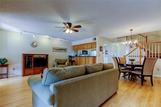 living room featuring ceiling fan with notable chandelier, light hardwood / wood-style floors, and a textured ceiling