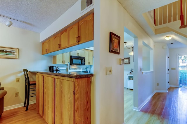 kitchen with a breakfast bar area, range, a textured ceiling, light hardwood / wood-style flooring, and track lighting