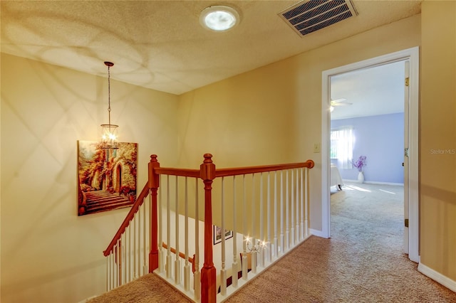 hallway featuring an inviting chandelier, carpet floors, and a textured ceiling