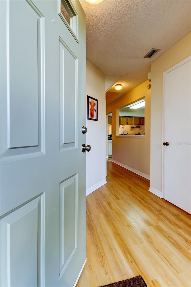 hall with light wood finished floors, visible vents, a textured ceiling, and baseboards