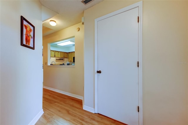 corridor featuring visible vents, baseboards, and light wood finished floors