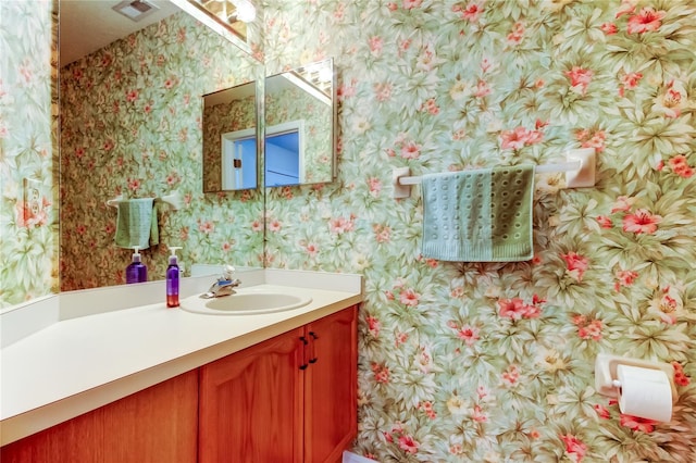 bathroom with visible vents, vanity, and wallpapered walls