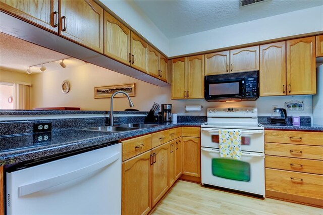 kitchen featuring light wood finished floors, dark stone countertops, white appliances, a textured ceiling, and a sink