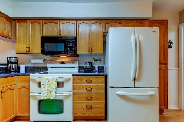 kitchen featuring dark stone counters, white appliances, and brown cabinets