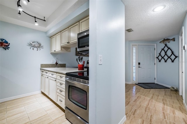 kitchen featuring cream cabinets, rail lighting, a textured ceiling, and appliances with stainless steel finishes