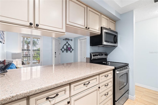 kitchen with appliances with stainless steel finishes, light stone countertops, and cream cabinetry