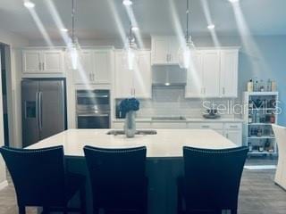 kitchen with tasteful backsplash, stainless steel appliances, an island with sink, and white cabinets