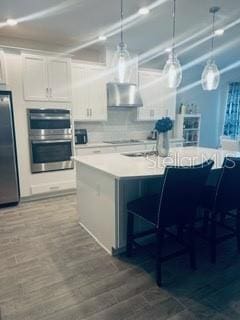 kitchen featuring range hood, decorative light fixtures, stainless steel appliances, and white cabinets