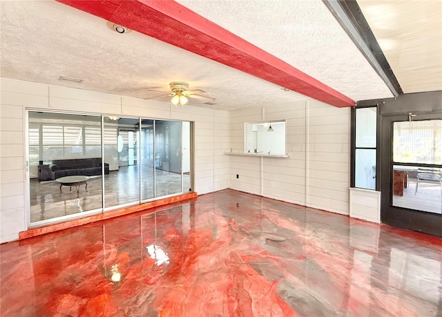 unfurnished living room with ceiling fan, beamed ceiling, and a textured ceiling