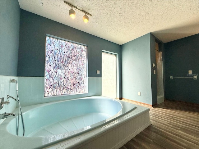 bathroom featuring tiled tub, hardwood / wood-style floors, and a textured ceiling