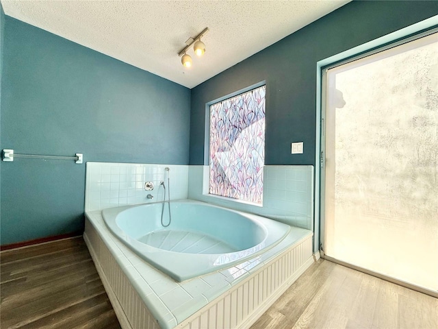 bathroom featuring a relaxing tiled tub, hardwood / wood-style flooring, rail lighting, and a textured ceiling