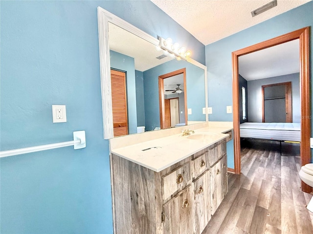 bathroom with toilet, a textured ceiling, vanity, hardwood / wood-style flooring, and ceiling fan