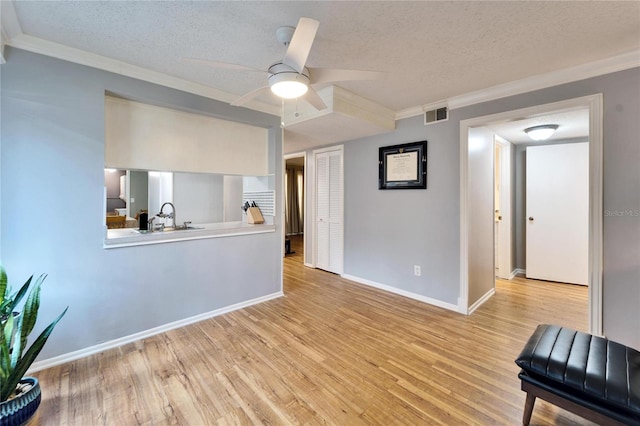 living room with ceiling fan, ornamental molding, a textured ceiling, and light wood-type flooring