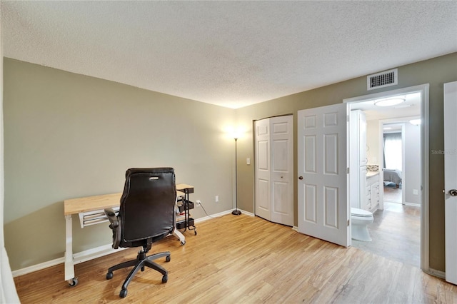 home office with a textured ceiling and light hardwood / wood-style flooring