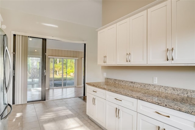 kitchen with white cabinetry, light stone countertops, light tile patterned floors, and stainless steel fridge